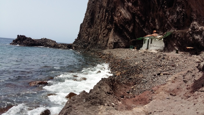 ein altes, kleines, weisses Haus am Strand, welches in die hoch aufragende Klippe hineingebaut ist