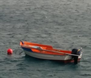 ein kleines Boot mit roter Boje schwimmt auf dem Meer, ausser Wasser sieht man im HIntergrund nur einen schmalen Weg in der Mitte zwischen zwei Felswänden durch