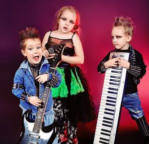 drei punkig gekleidete und frisierte Kinder spielen auf Rockgitarristen mit E-Gitarre und Keyboard