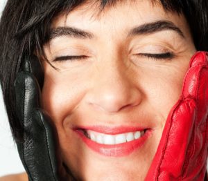 ein Porträt einer mit geschlossenen Augen glücklich strahlenden Frau mit dunklen kurzen Haaren,