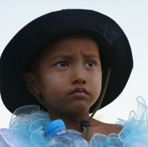 ein Mädchen aus Myanmar mit Hut mit Krempe schaut kritisch und ernst ins Weite, Porträt