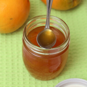 ein offenes Orangenmarmelade-Glas, grüner Untergrund