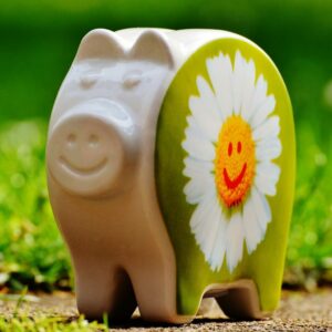 ein lächelndes Keramikschwein, um die Mitte dünn und seitlich kugelrund mit einer Sonnenblume im Runden, im Hintergrund ist Wiese